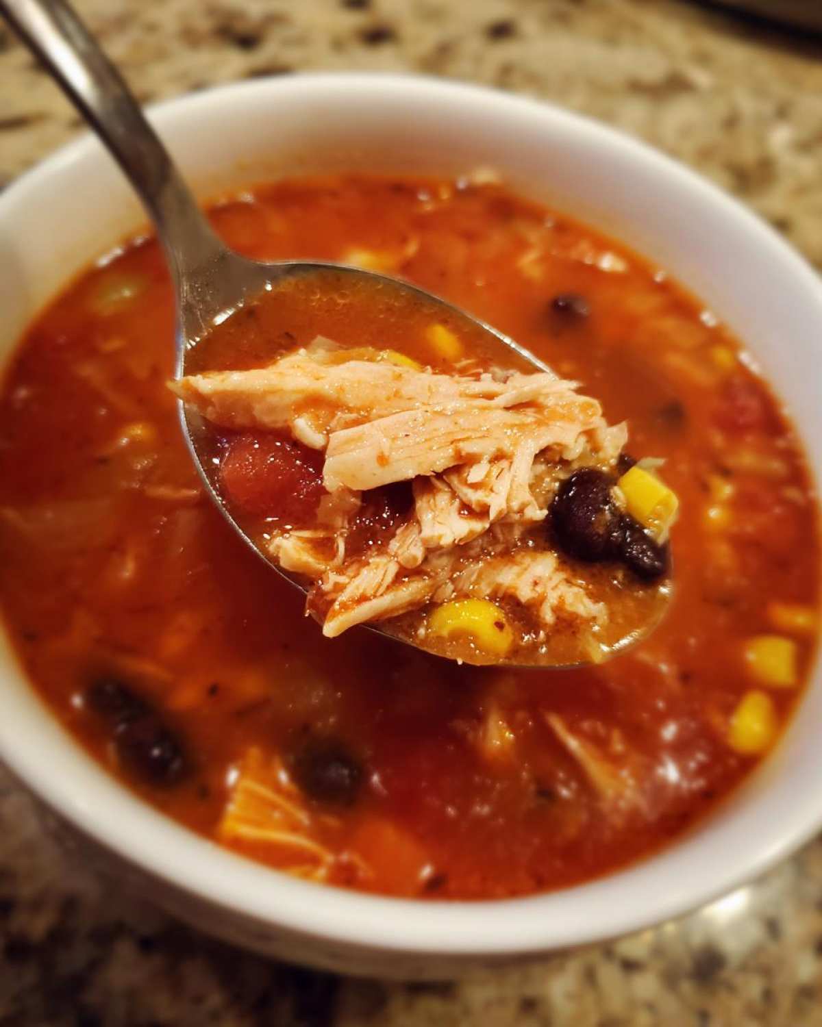 A spoonful of shredded chicken, corn, and black beans lifted from a bowl of Instant Pot Chicken Tortilla Soup.