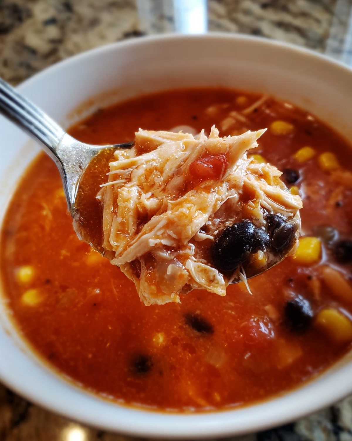 Close-up of a spoonful of Instant Pot Chicken Tortilla Soup showing shredded chicken, black beans, and corn in a rich broth.
