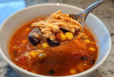 A spoonful of Instant Pot Chicken Tortilla Soup showing shredded chicken, black beans, and corn being lifted from a white bowl.
