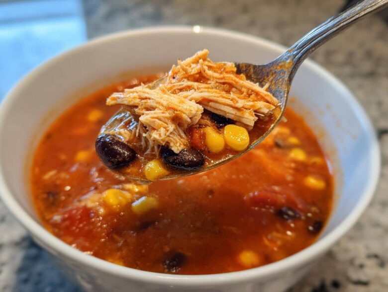 A spoonful of Instant Pot Chicken Tortilla Soup showing shredded chicken, black beans, and corn being lifted from a white bowl.