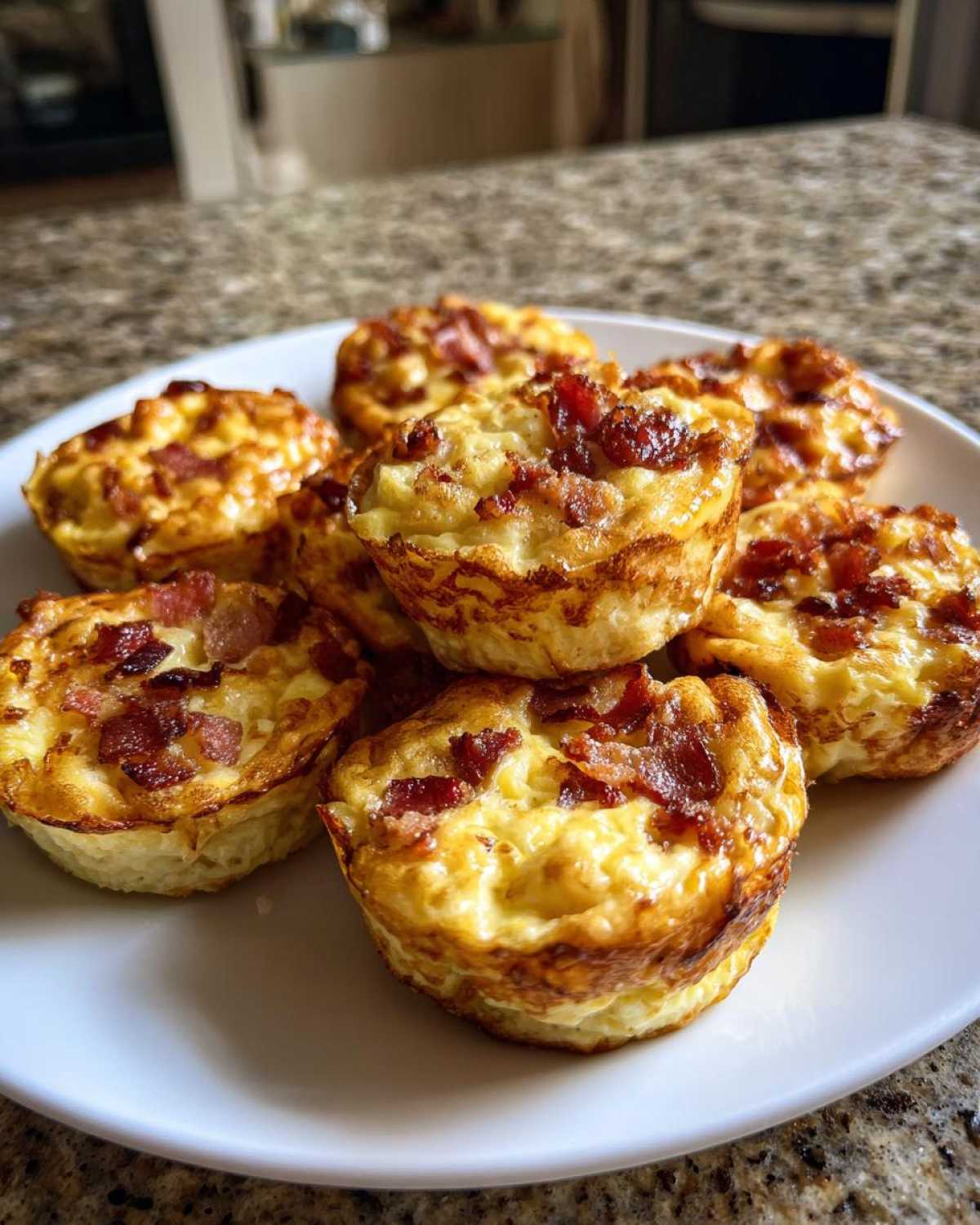 A plate piled high with freshly baked Keto Bacon and Egg Muffins, topped with crispy bacon bits.