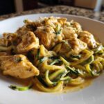 Close-up of Keto Chicken Alfredo featuring chunks of seasoned chicken breast over zucchini noodles coated in a creamy sauce.