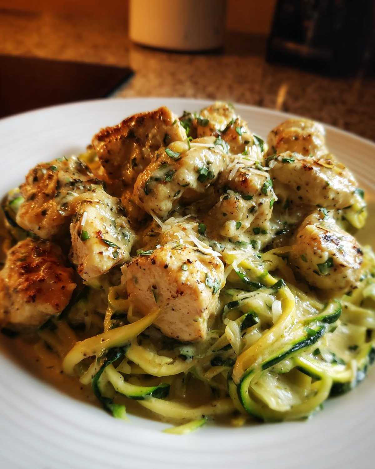 Close-up of Keto Chicken Alfredo featuring pan-seared chicken chunks over zucchini noodles in a creamy sauce.