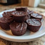 A close-up of several rich, dark chocolate Keto Chocolate Peanut Butter Fat Bombs arranged on a white plate.