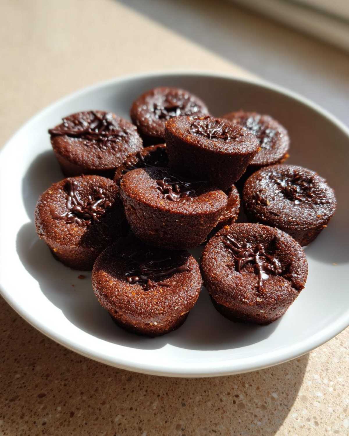 A white plate holds several small, dark brown Keto Chocolate Peanut Butter Fat Bombs topped with a chocolate drizzle.