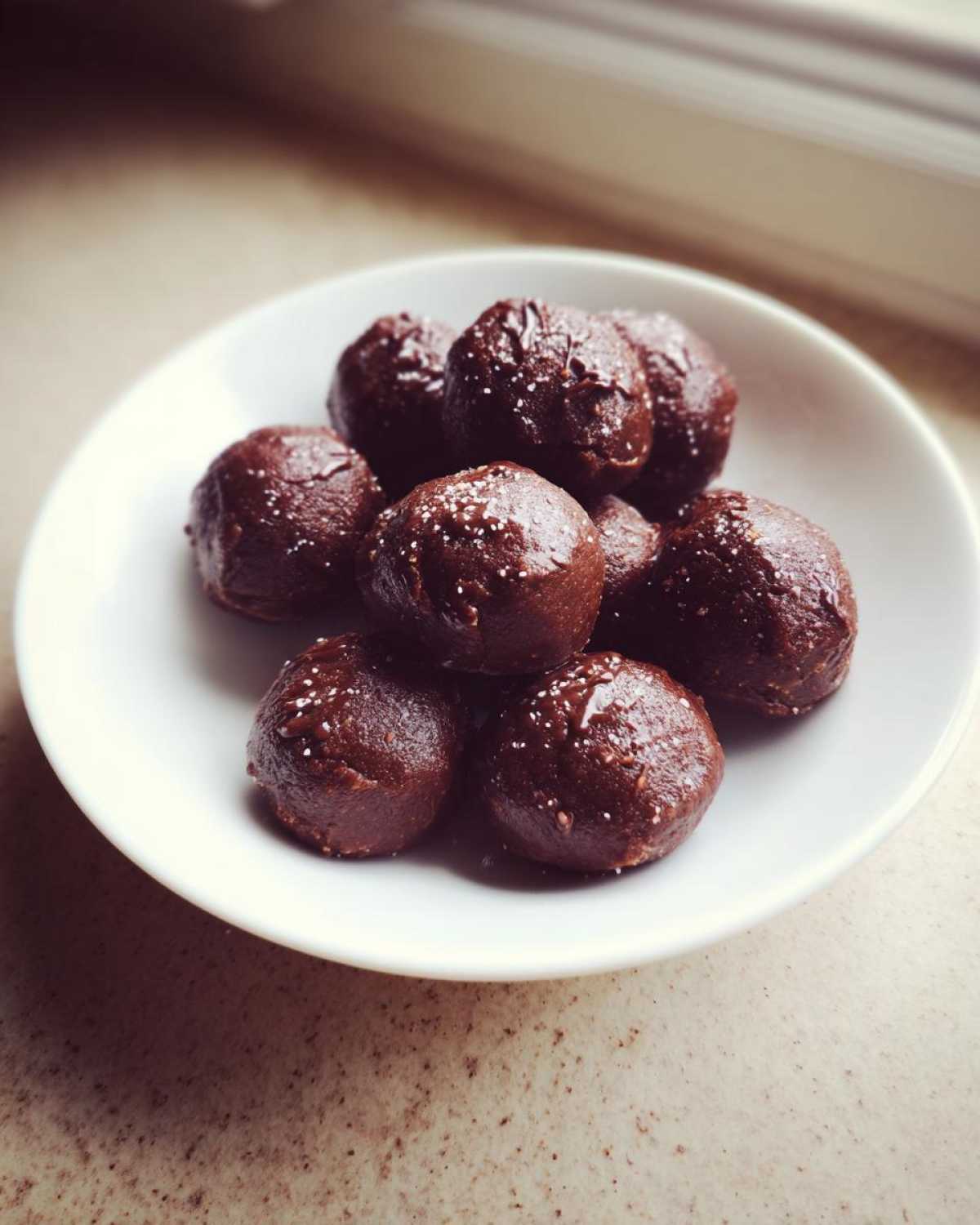 A small white bowl filled with rich, dark Keto Chocolate Peanut Butter Fat Bombs sprinkled with sea salt.