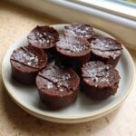 Close-up of seven rich, dark Keto Chocolate Peanut Butter Fat Bombs topped with sea salt flakes.