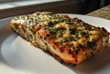 A perfectly cooked fillet of Keto Garlic Butter Salmon topped with melted cheese and herbs, resting on a white plate.