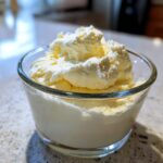 A glass bowl filled with light yellow Keto Lemon Cheesecake Mousse, topped with whipped cream.