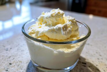A glass bowl filled with light yellow Keto Lemon Cheesecake Mousse, topped with whipped cream.