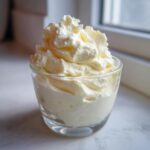 A glass filled with fluffy, white whipped topping, likely the Keto Lemon Cheesecake Mousse.