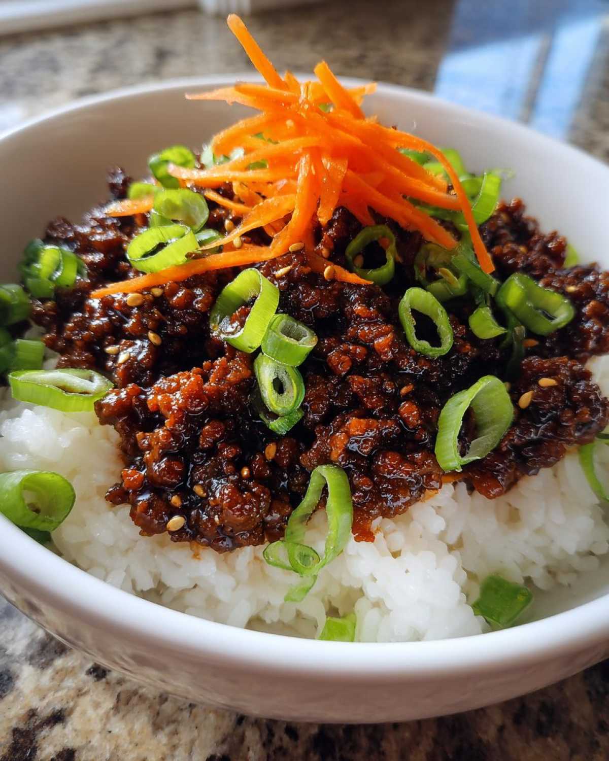 Close-up of a Korean Ground Beef Bulgogi Bowl featuring savory ground beef over white rice, garnished with shredded carrots and green onions.