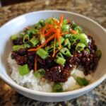 A close-up of a Korean Ground Beef Bulgogi Bowl featuring saucy ground beef over white rice, topped with green onions and shredded carrots.
