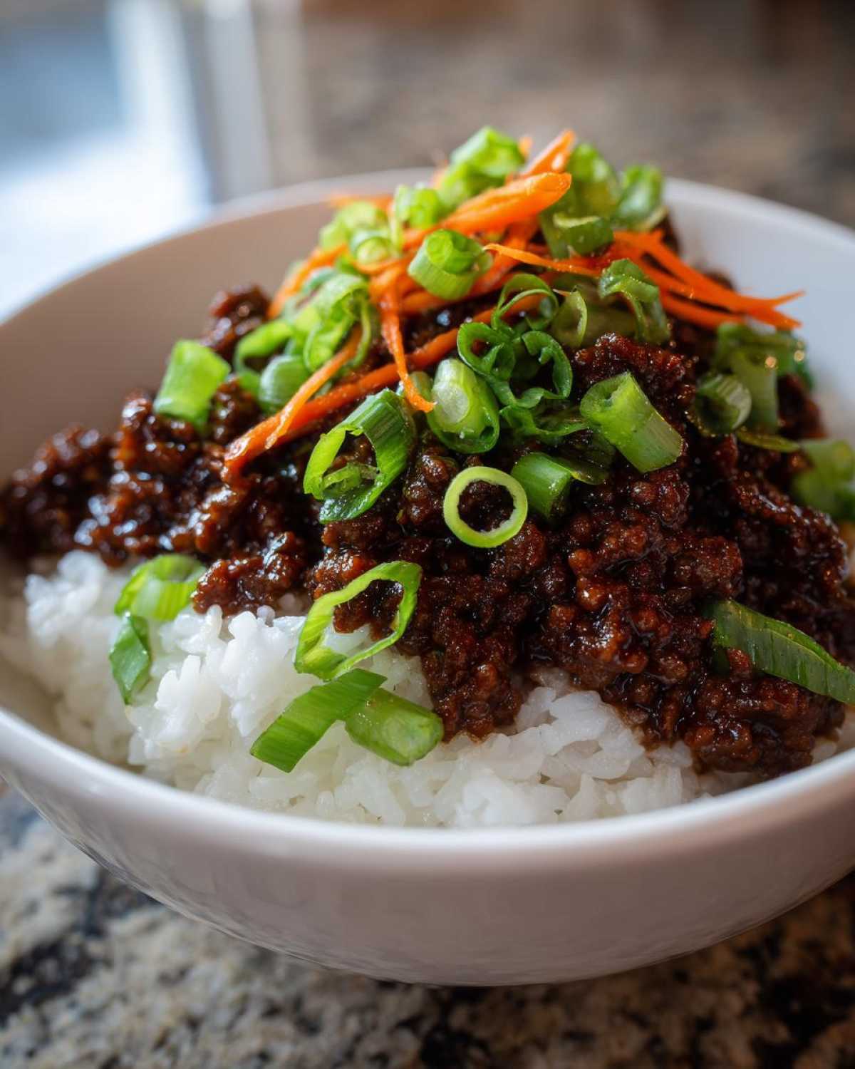 A close-up of Korean Ground Beef Bulgogi Bowls featuring savory ground beef over white rice, topped with sliced green onions and shredded carrots.