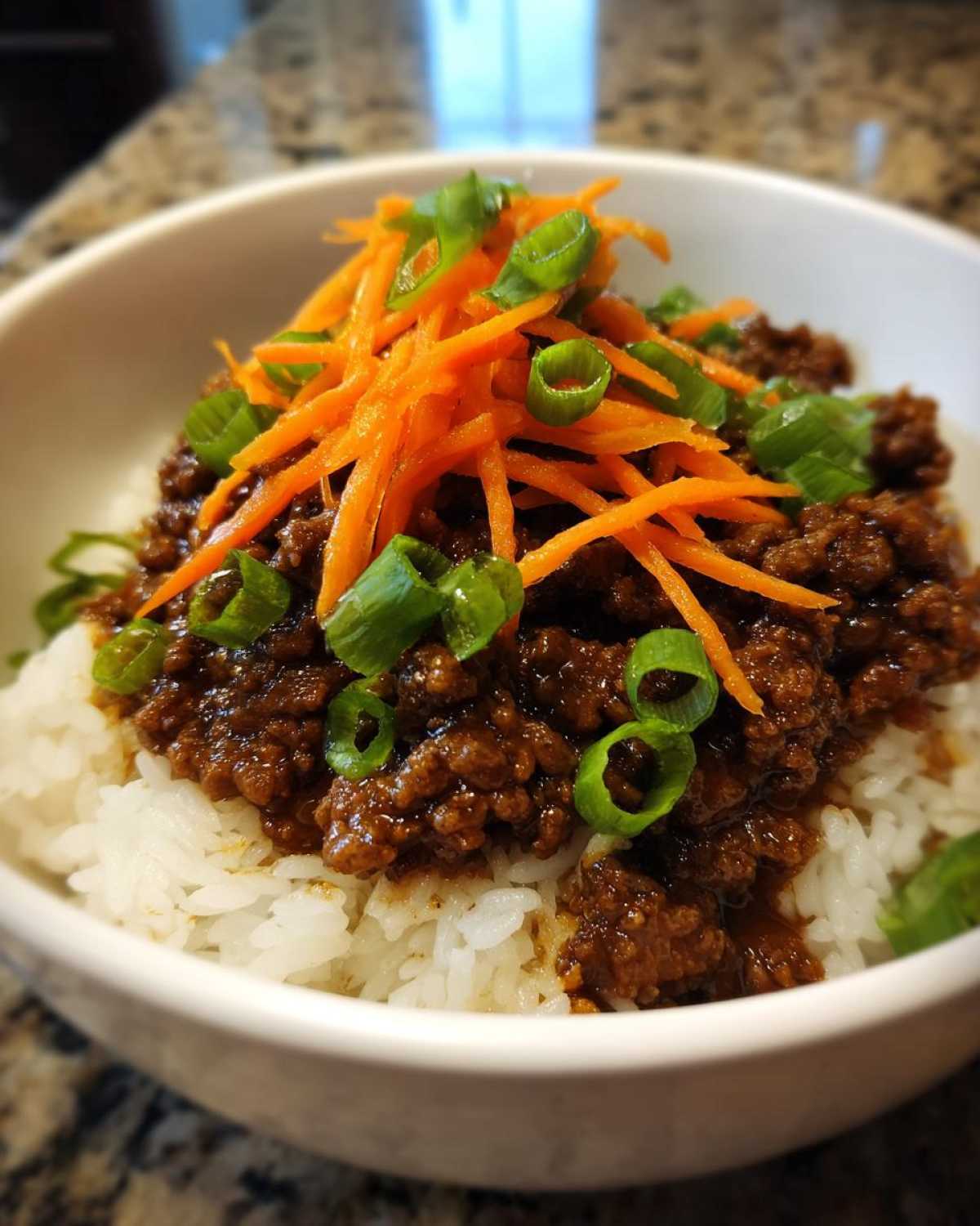 Close-up of Korean Ground Beef Bulgogi Bowls featuring savory ground beef over white rice, topped with shredded carrots and green onions.