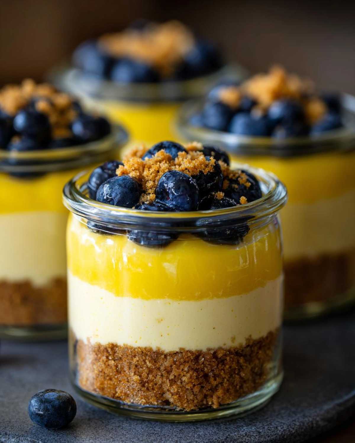 Close-up of a layered Lemon Blueberry Cheesecake Jars dessert showing graham cracker crust, cream cheese, lemon curd, and fresh blueberries.