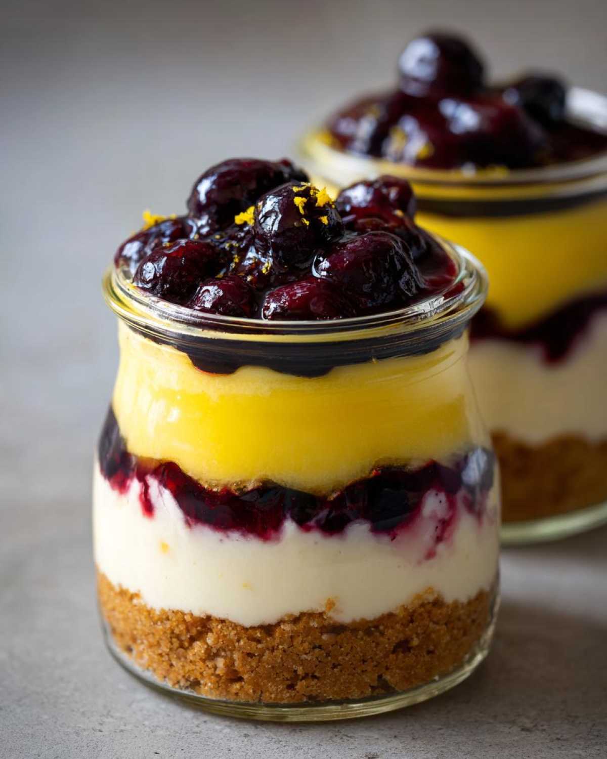 Close-up of a layered Lemon Blueberry Cheesecake Jars dessert with graham cracker crust, cream cheese, lemon curd, and blueberry topping.