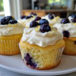 Close-up of several Lemon Blueberry Cupcakes with Cream Cheese Frosting, topped with fresh blueberries and lemon zest.