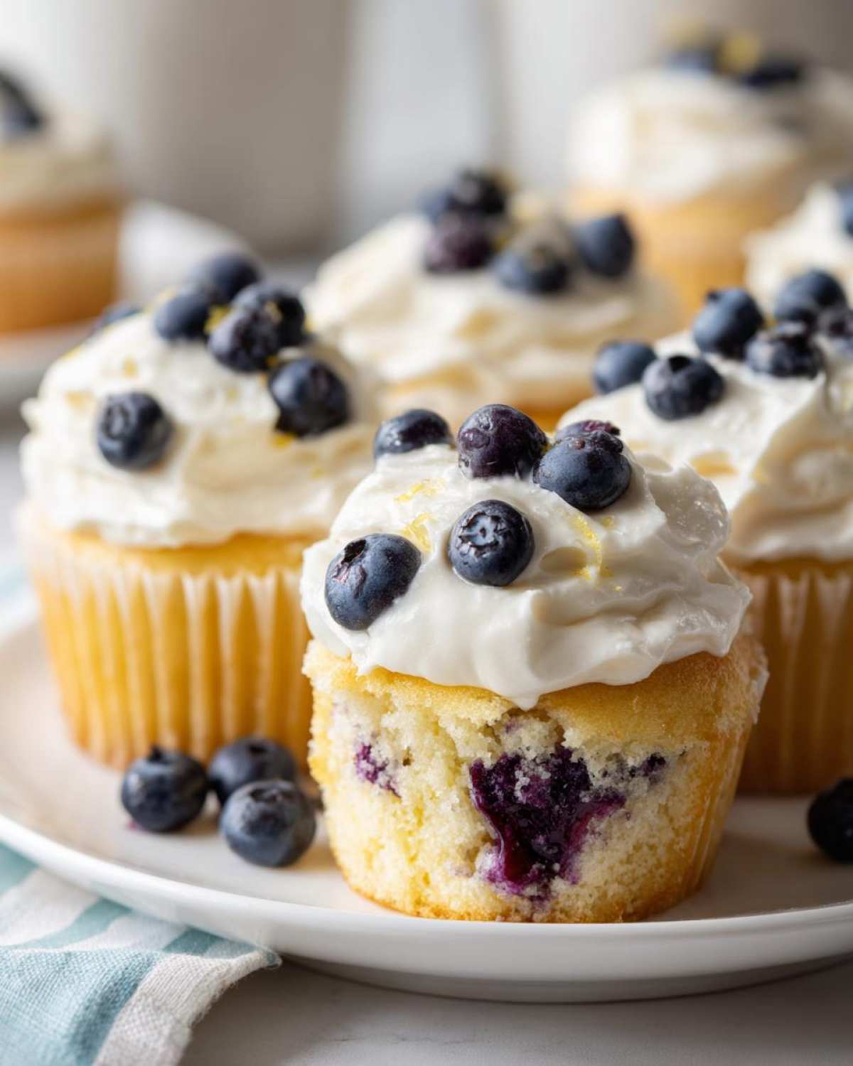 A close-up of a Lemon Blueberry Cupcakes with Cream Cheese Frosting, showing the moist interior and fresh blueberries.
