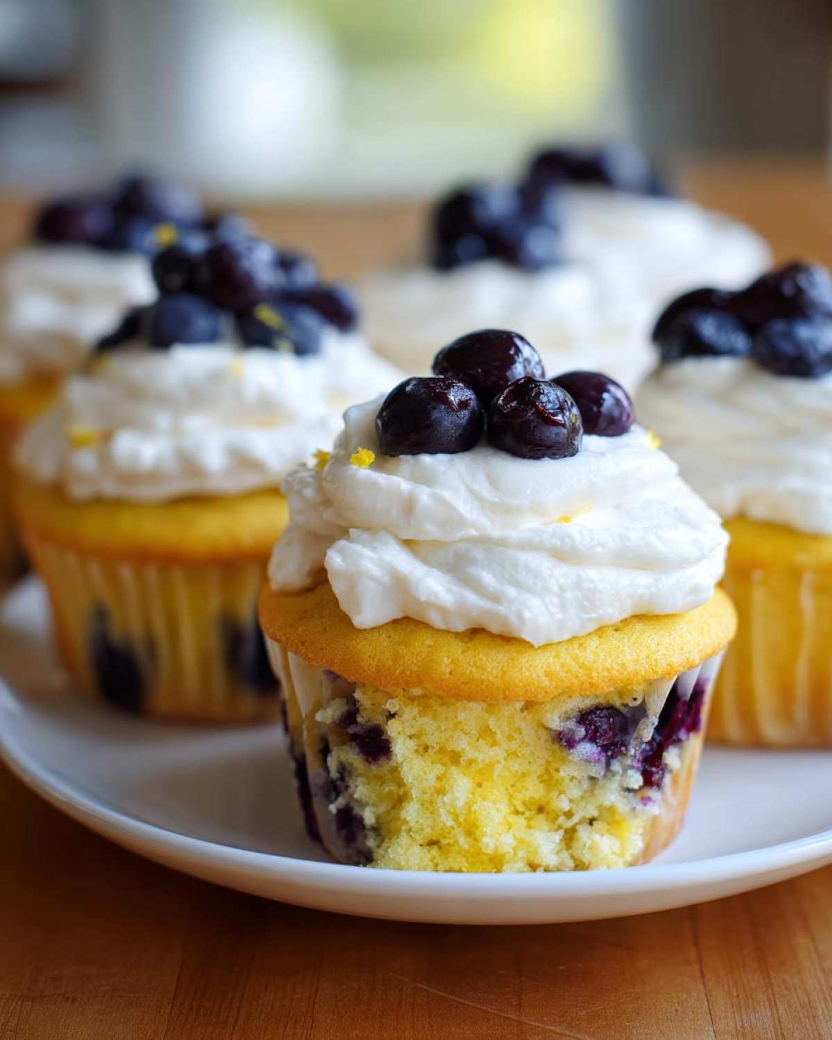 A close-up of a Lemon Blueberry Cupcake with cream cheese frosting, topped with fresh blueberries and lemon zest.
