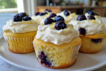 Close-up of several Lemon Blueberry Cupcakes with Cream Cheese Frosting, topped with fresh blueberries and lemon zest.