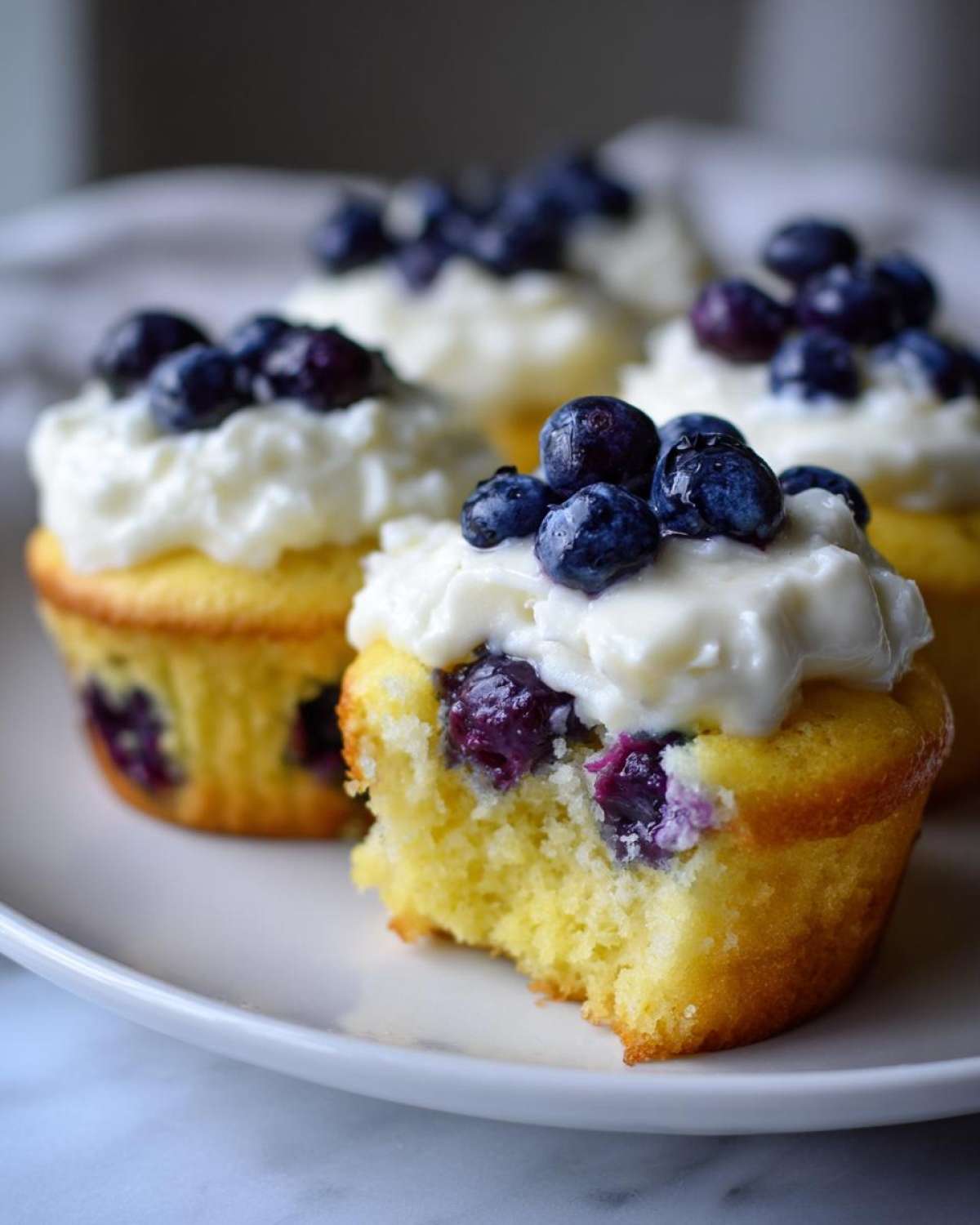 Close-up of a Lemon Blueberry Cupcake with cream cheese frosting and fresh blueberries, showing a bite taken out.