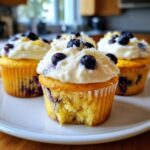 Close-up of a Lemon Blueberry Cupcake with cream cheese frosting, showing a bite taken out of the moist cake.