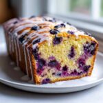 Close-up of a slice of moist Lemon Blueberry Yogurt Loaf drizzled with white glaze.