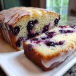 Close-up of a moist Lemon Blueberry Yogurt Loaf, sliced to show blueberries and topped with a thick lemon glaze.