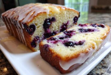 Close-up of a moist Lemon Blueberry Yogurt Loaf, sliced to show blueberries and topped with a thick lemon glaze.