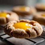 Close-up of a textured, baked Lemon Curd Thumbprint Cookie filled with bright yellow lemon curd, resting on a wire cooling rack.
