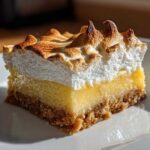 A close-up of a single square of Lemon Meringue Pie Bars showing graham cracker crust, lemon filling, and torched meringue.