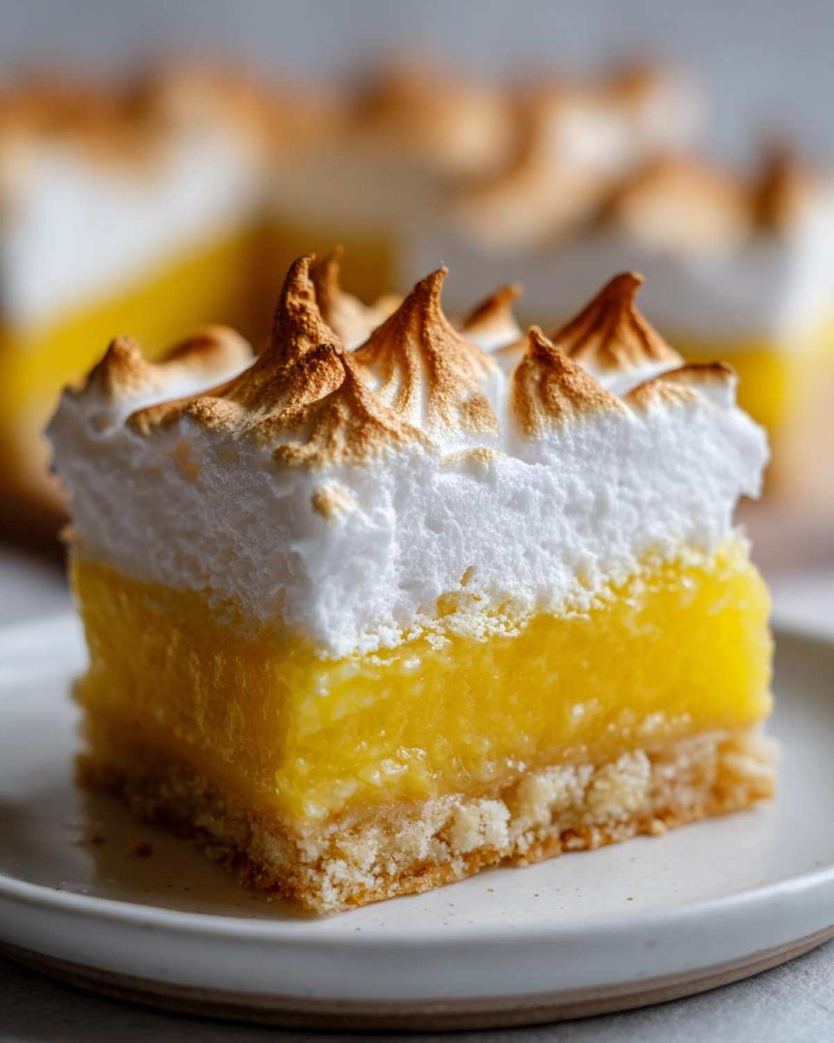 Close-up of a single serving of Lemon Meringue Pie Bars showing a shortbread crust, bright yellow lemon filling, and torched meringue topping.