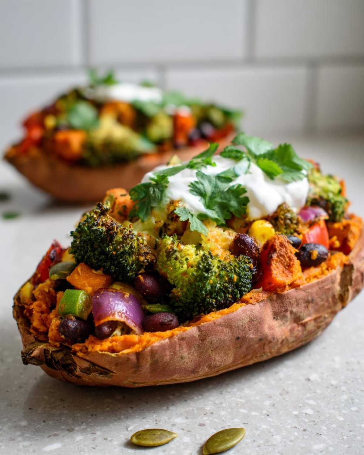 Close-up of a Loaded Veggie Stuffed Sweet Potatoes overflowing with roasted vegetables and topped with sour cream and cilantro.