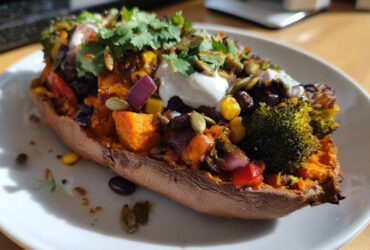 A vibrant Loaded Veggie Stuffed Sweet Potatoes half filled with roasted vegetables, topped with sour cream and cilantro.