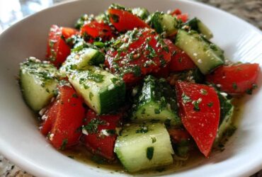 Close-up of a vibrant Mediterranean Cucumber Tomato Salad tossed with herbs and dressing in a white bowl.