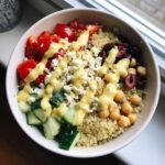 Overhead view of a Mediterranean Quinoa Bowl with lemon tahini sauce drizzled over quinoa, tomatoes, cucumbers, feta, and chickpeas.