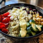 Close-up of a vibrant Mediterranean Quinoa Bowl featuring quinoa, feta, tomatoes, cucumbers, chickpeas, and lemon tahini sauce.