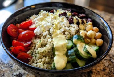 Close-up of a vibrant Mediterranean Quinoa Bowl featuring quinoa, feta, tomatoes, cucumbers, chickpeas, and lemon tahini sauce.