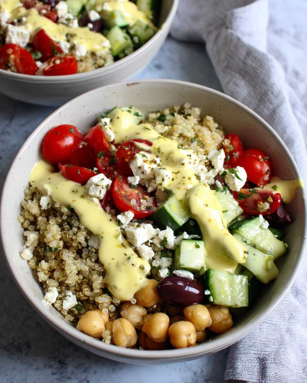 Close-up of a Mediterranean Quinoa Bowl with lemon tahini sauce drizzled over quinoa, tomatoes, cucumbers, feta, and chickpeas.