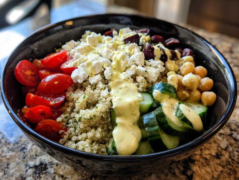 Close-up of a vibrant Mediterranean Quinoa Bowl featuring quinoa, feta, tomatoes, cucumbers, chickpeas, and lemon tahini sauce.