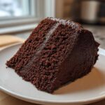 A thick, moist slice of dark chocolate Gluten-Free Chocolate Cake with rich frosting on a white plate.