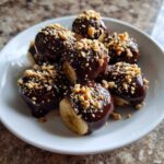 A white plate filled with No-Bake Chocolate Covered Banana Bites topped with chopped peanuts.