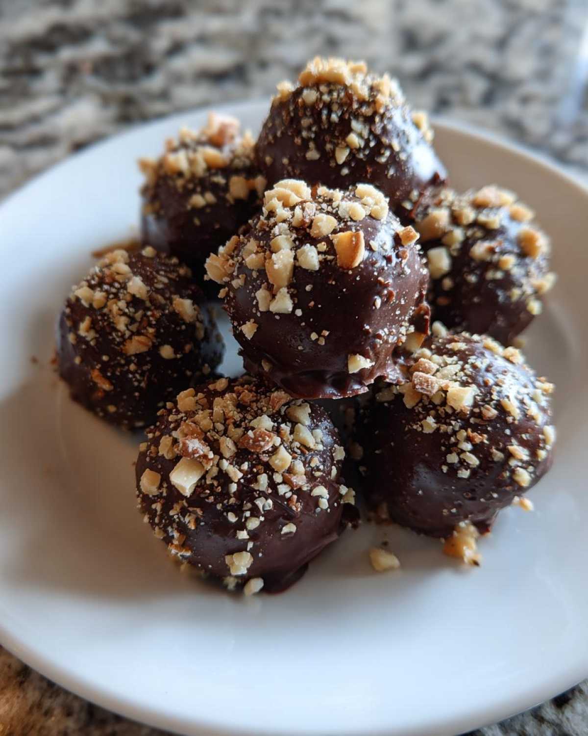 A pile of No-Bake Chocolate Covered Banana Bites dipped in dark chocolate and topped with chopped nuts.