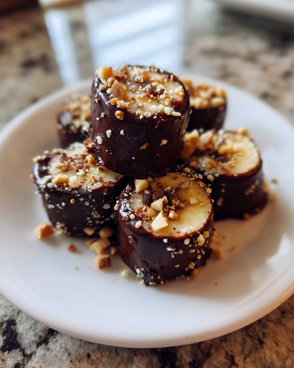 Close-up of No-Bake Chocolate Covered Banana Bites dipped in dark chocolate and topped with chopped nuts.