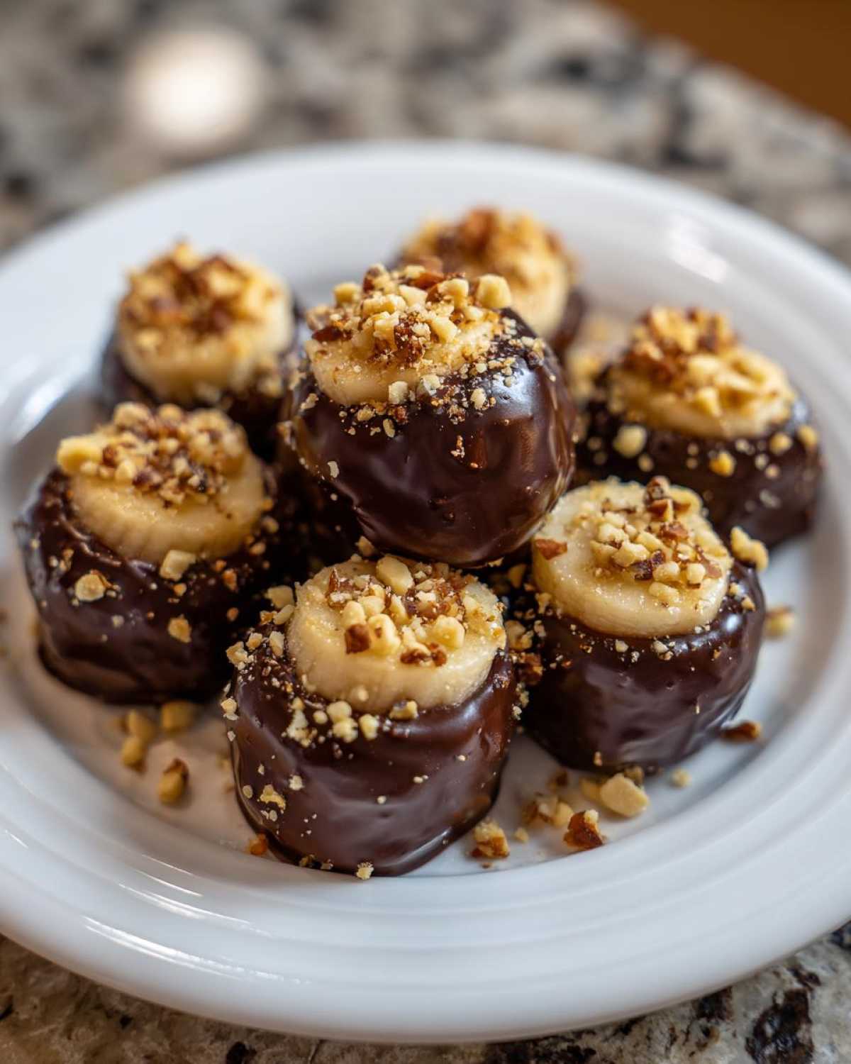 Close-up of several No-Bake Chocolate Covered Banana Bites topped with chopped nuts on a white plate.