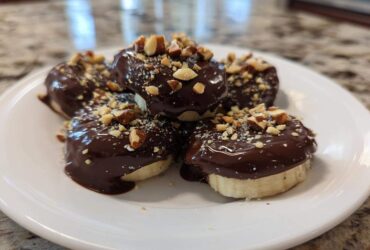 A stack of No-Bake Chocolate Covered Banana Bites dipped in dark chocolate and topped with chopped nuts on a white plate.