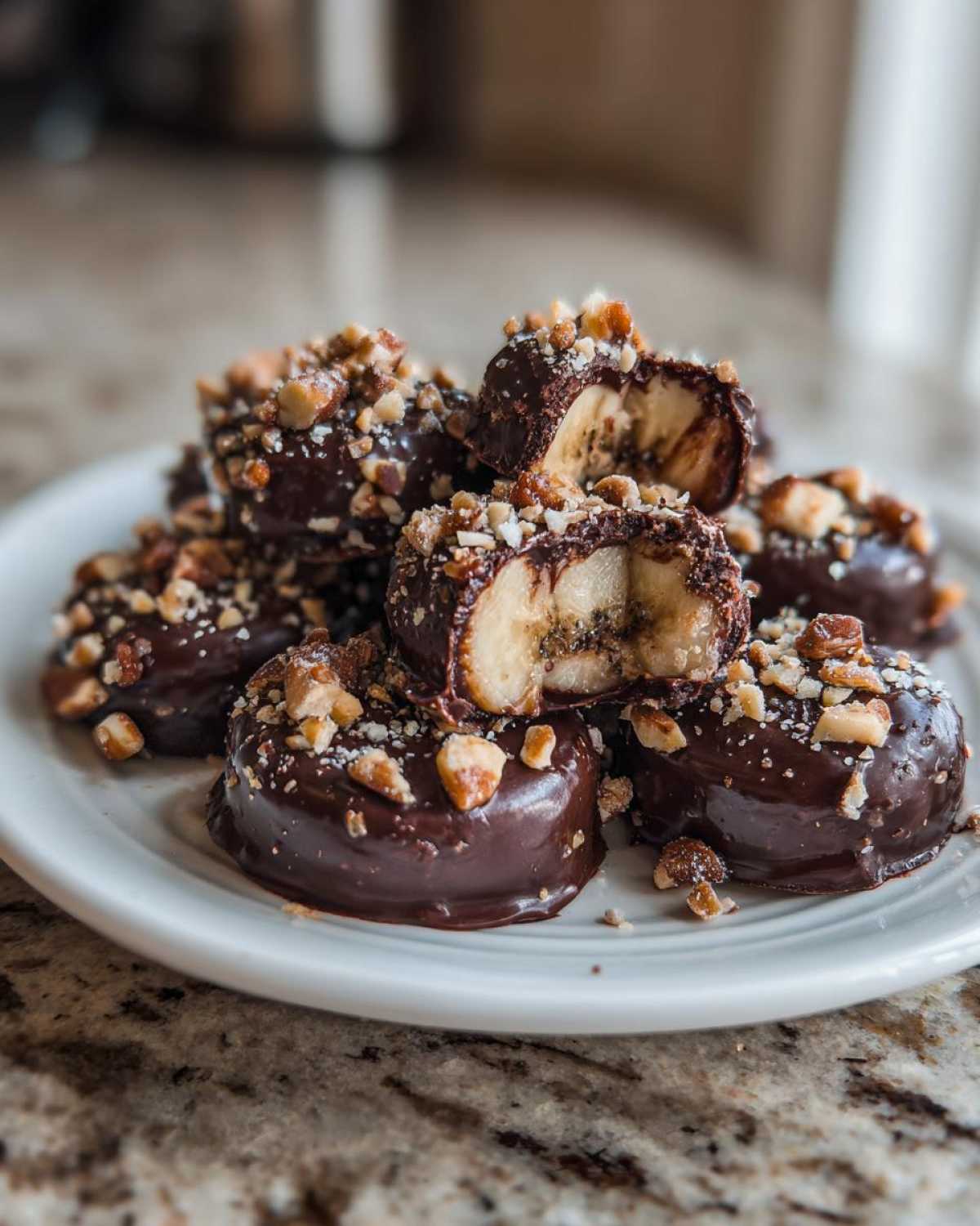 A pile of No-Bake Chocolate Covered Banana Bites dipped in dark chocolate and topped with chopped nuts.