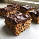 A close-up of a square No-Bake Chocolate Peanut Butter Oat Bars showing the textured oat base and thick chocolate topping.