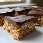Close-up of several squares of No-Bake Chocolate Peanut Butter Oat Bars stacked on a white plate.
